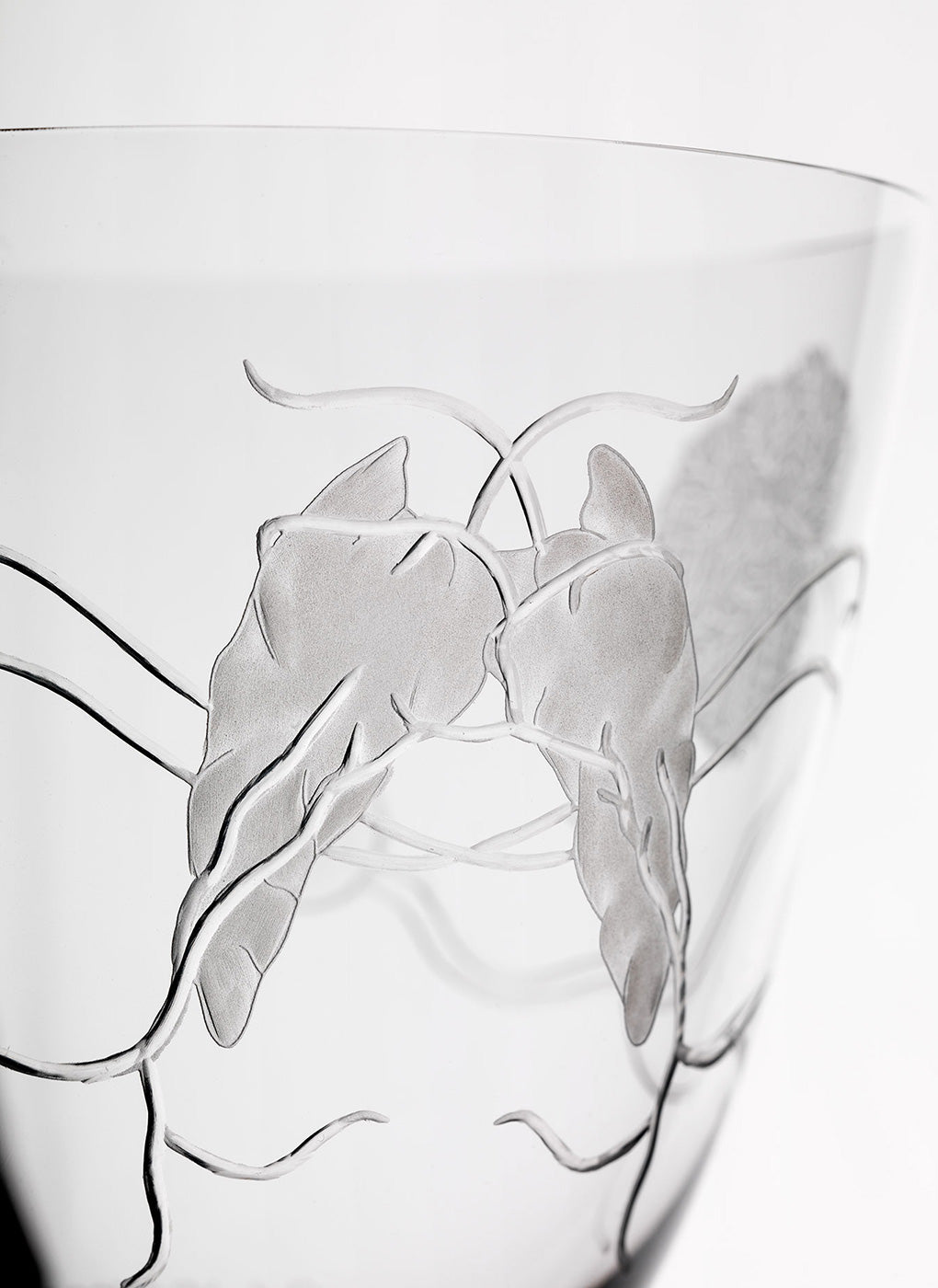 Close-up of a Goblets of Humanity glass bowl by Lobmeyr, engraved by Nives Widauer. Its intricate leaf and branch patterns create an elegant, delicate look on the smooth, transparent surface.