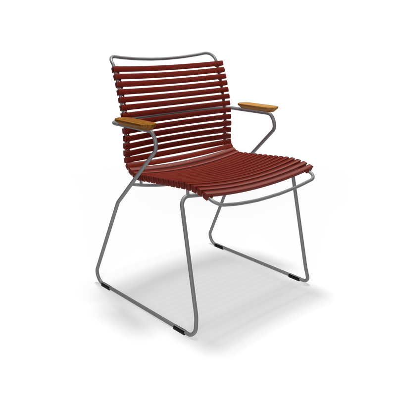 The Click Dining Chair with Armrest by Houe is a modern outdoor chair featuring a sleek black metal sled base, weather-resistant red slatted seat and backrest, light wooden armrests, and durable plastic lamellas.