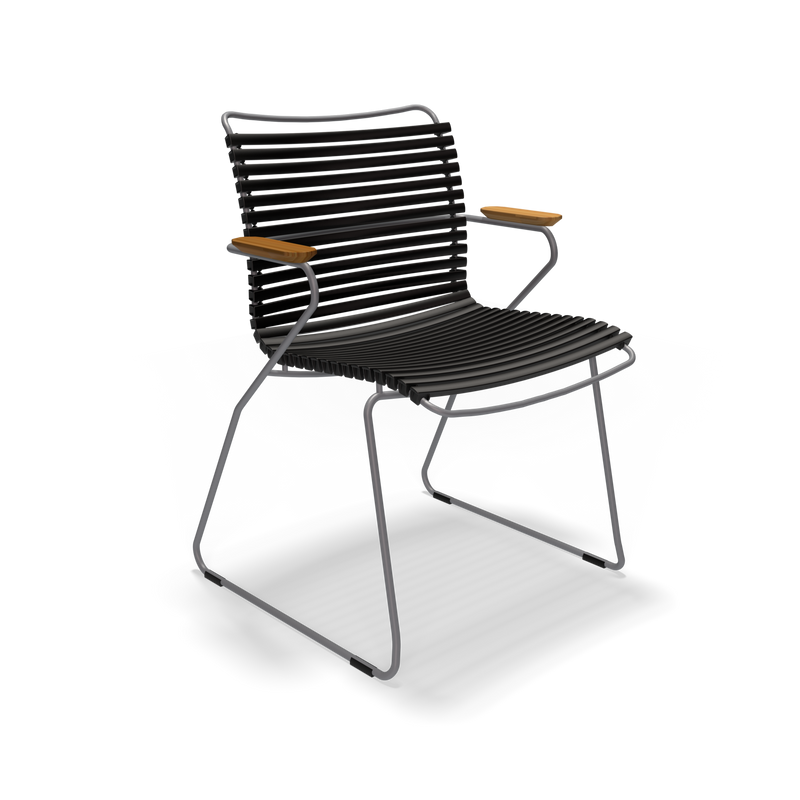 The Click Dining Chair with Armrest by Houe features a sleek black metal frame with a slatted seat and backrest enhanced with UV protection. It includes wooden armrest accents and thin, weather-resistant legs for a minimalist, contemporary look.