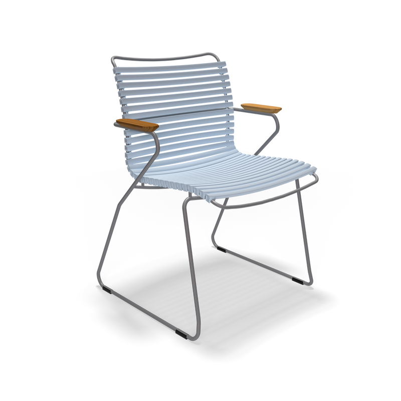 The Click Dining Chair with Armrest by Houe is a modern metal chair featuring horizontal slats on the seat and backrest, thin angled legs, and wooden armrests. Its sleek, minimalist, weather-resistant design makes it ideal for outdoor use, elegantly combining durability with style.