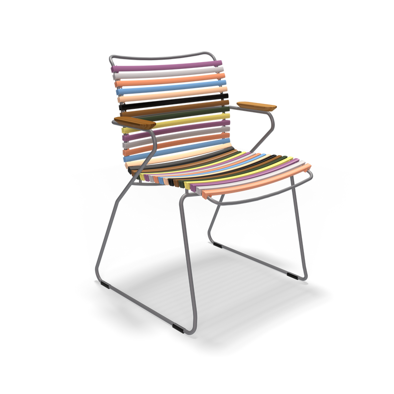 The Click Dining Chair with Armrest by Houe features a sleek metal frame, colorful UV-protected horizontal slats for the seat and backrest, wooden armrests, and a modern bright design. The weather-resistant chair stands out against a black background.