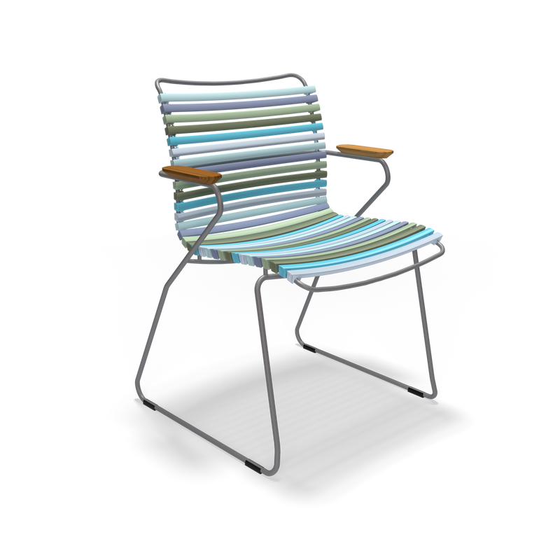 The Click Dining Chair with Armrest by Houe features a sleek, weather-resistant metal frame and wooden armrests. Its seat and back have UV-protected parallel bands in green, blue, and gray shades.
