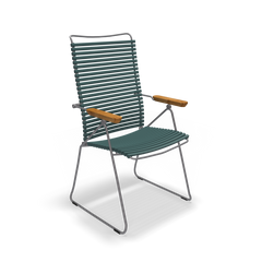 The Click Position Chair by Houe features a modern design with weather-resistant dark green slatted plastic lamellas, wooden armrests, and a thin metal frame with angled legs, making it perfect for any patio setting.