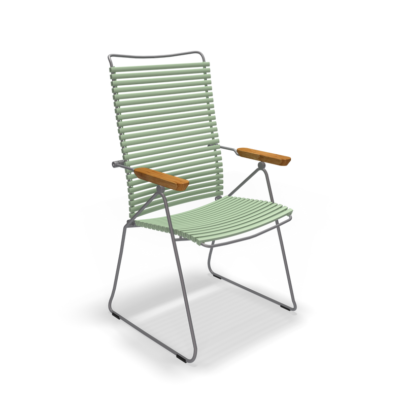 The Click Position Chair by Houe is a modern outdoor chair featuring a metal frame with light green, weather-resistant plastic lamellas on the seat and backrest. Wooden armrests provide a contrasting touch to its sleek, slatted design.