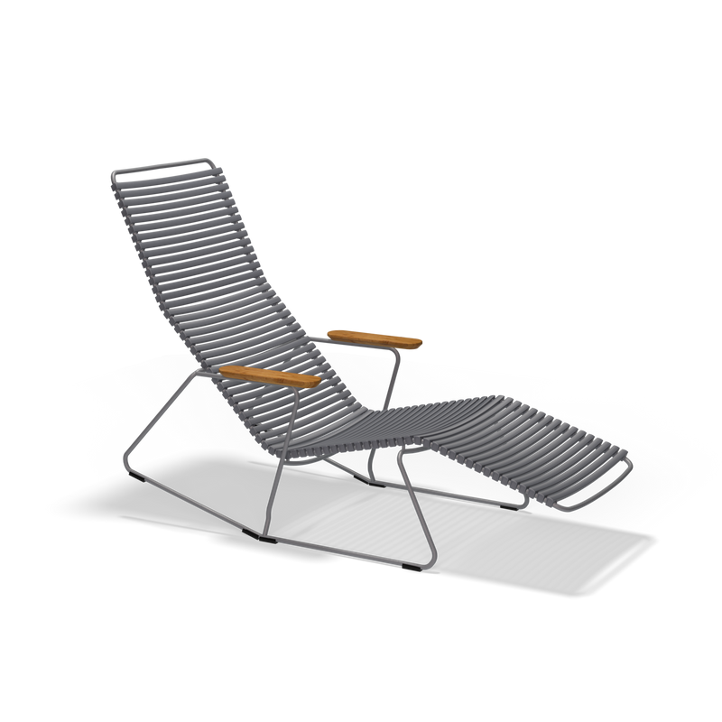 The Click Sunrocker by Houe is a contemporary outdoor reclining lounge chair with a minimalist design. It has a gray slatted plastic lamella seat and backrest, complemented by wooden armrests and a sleek metal frame, providing an angular modern style.