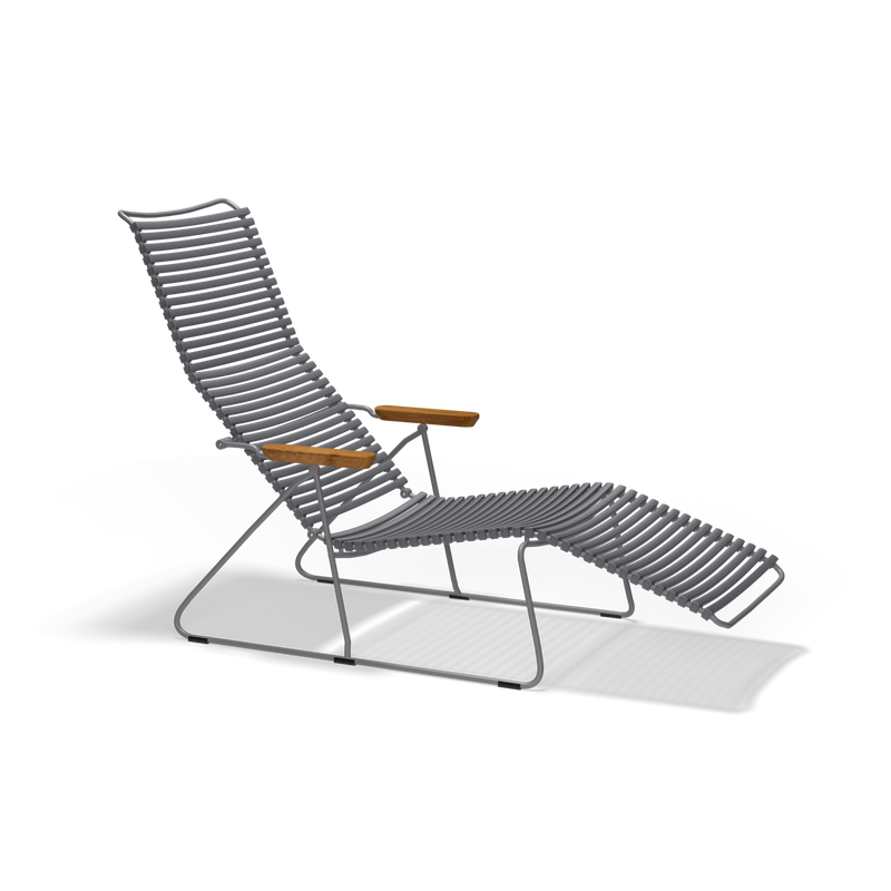 The Houe Click Sunlounger is a modern outdoor lounge chair featuring a sleek metal frame and horizontal slats for the seat and backrest, complemented by light wood armrests. This UV-protected, cushion-free seating stands stylishly against a black background.
