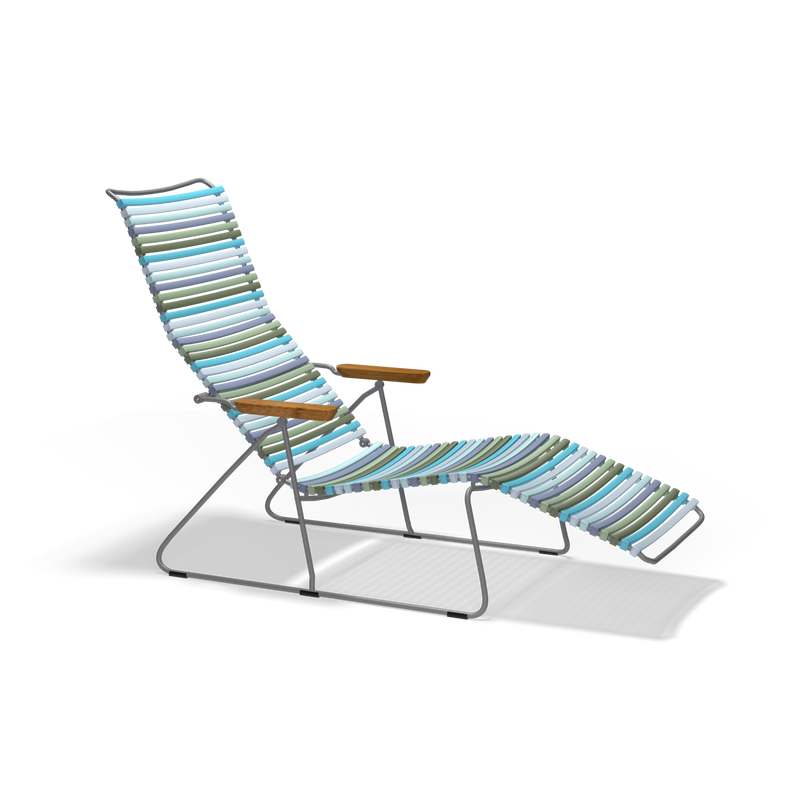 The Click Sunlounger by Houe is a colorful lounge chair with a metal frame and wooden armrests, designed for UV-protected outdoor use. It features cushion-free seating with an extended leg rest and high backrest in blue, green, and beige stripes on a black background.