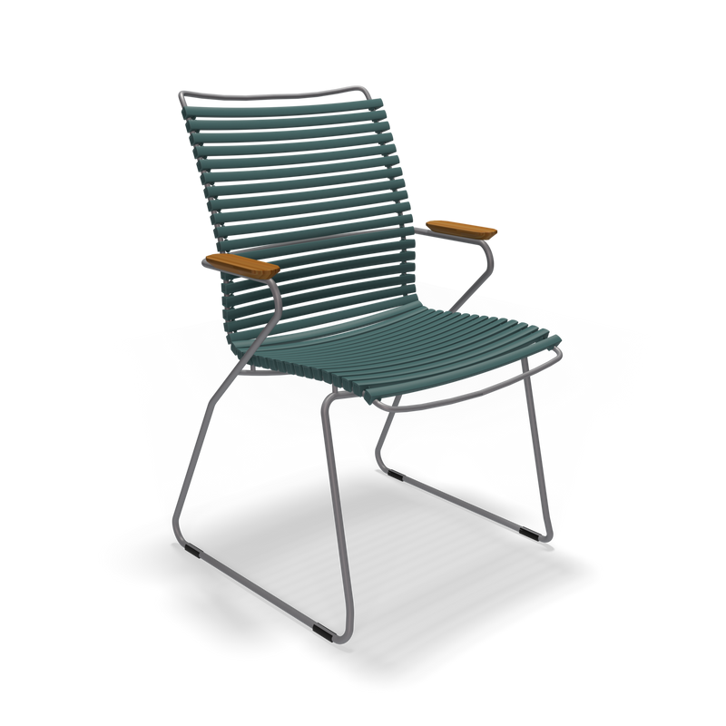 The Click Dining Chair with Armrest - Tall Back by Houe is a modern outdoor chair featuring a blue slatted design, wooden armrests, and a weather-resistant metal frame with a cantilever base. Its UV-protected materials offer lasting durability and minimalist style for outdoor comfort.