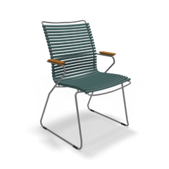 The Click Dining Chair with Armrest - Tall Back by Houe is a modern outdoor chair featuring a blue slatted design, wooden armrests, and a weather-resistant metal frame with a cantilever base. Its UV-protected materials offer lasting durability and minimalist style for outdoor comfort.