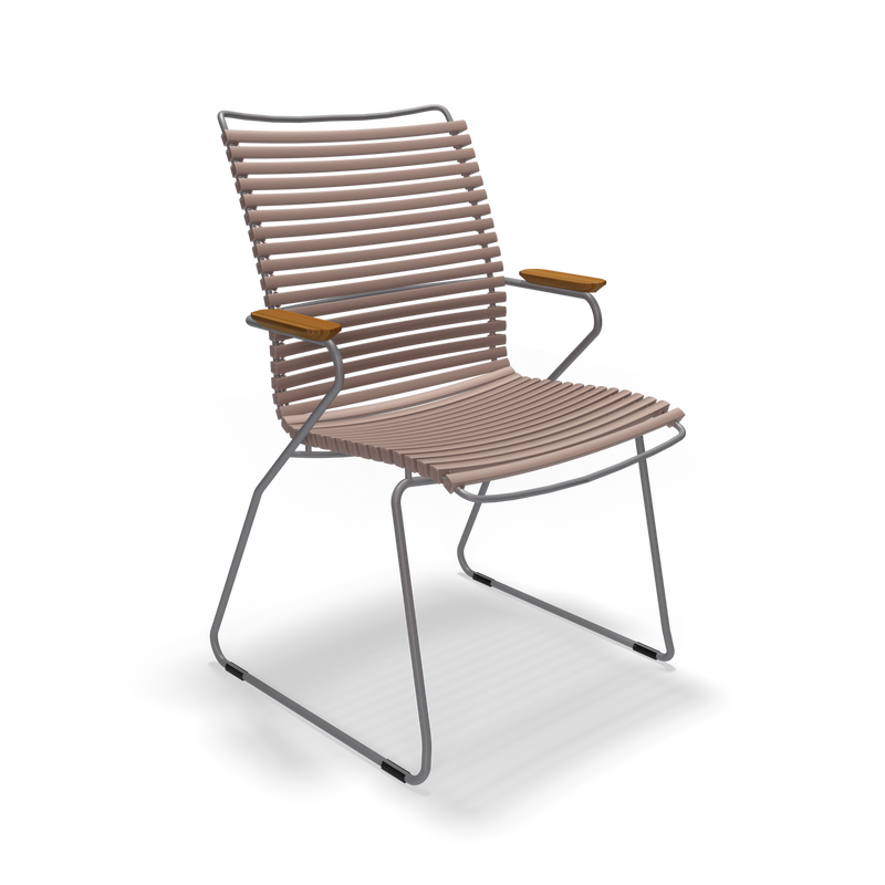 The Click Dining Chair with Armrest - Tall Back by Houe features a modern design with curved metal rods supporting horizontal slats for the seat and backrest. It has UV-protected wooden armrests and weather-resistant wireframe legs, all set against a sleek black background.