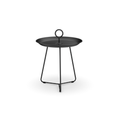 The Houe Eyelet Tray Table is a compact black metal side table made of powder-coated steel, featuring a round tray top with a loop handle. It stands on three slender legs connected by a triangular base support.