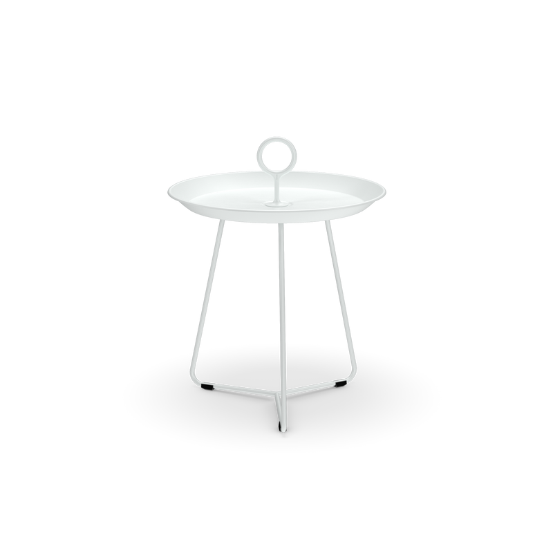 The Eyelet Tray Table by Houe is a small, white, round side table made from powder-coated steel. It has a circular handle on top and stands on three slender legs connected by a triangular base, set against a solid black background.
