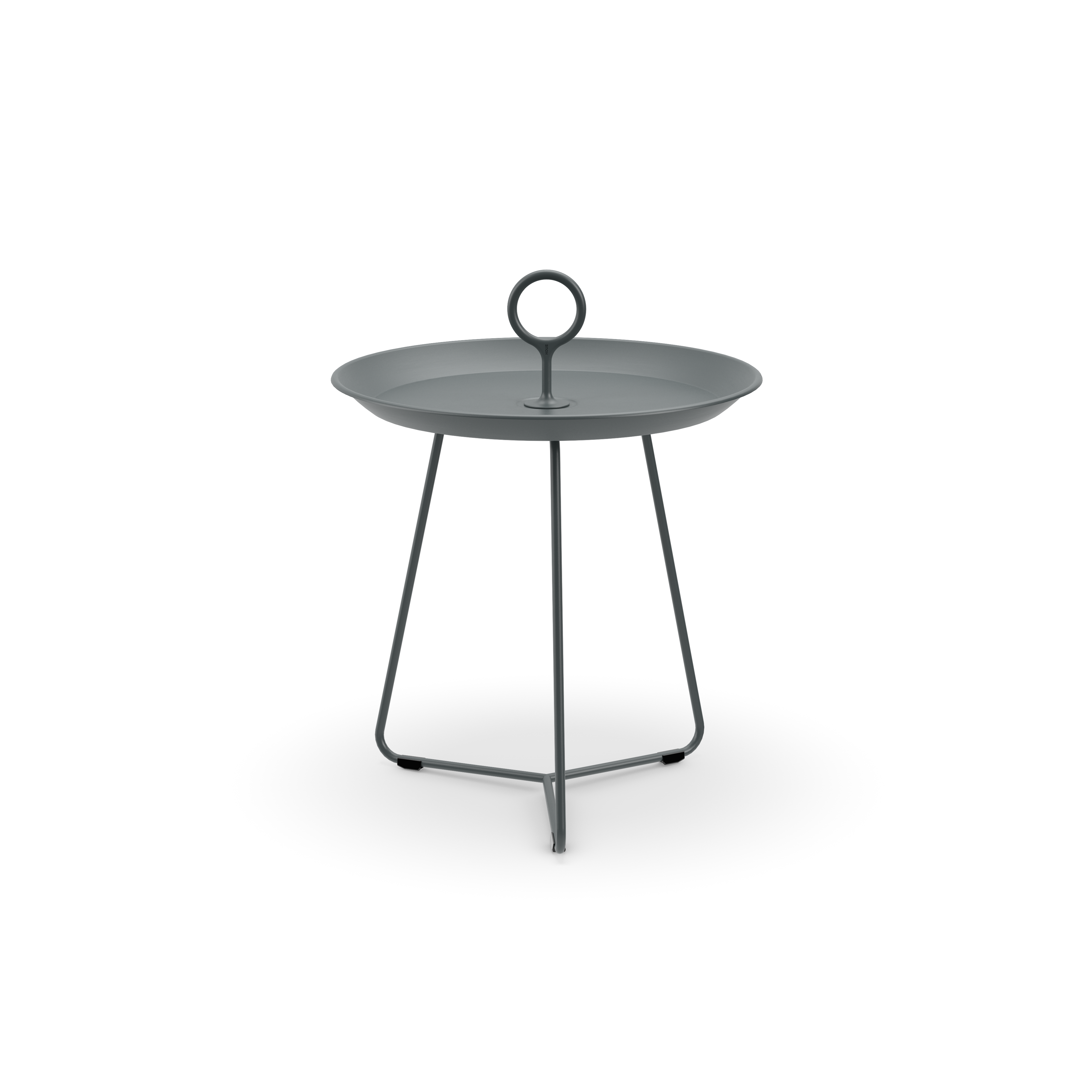 The Eyelet Tray Table by Houe is a minimalist piece with a round, dark gray metal surface and loop handle, crafted from powder-coated steel. It stands elegantly on three slender legs in a tripod base against a plain black background.