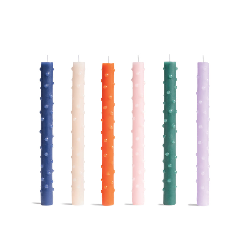 Six tall, textured &Klevering candles stand against a white backdrop in blue, cream, orange, pink, green, and lavender with raised dot patterns. Their vibrant design makes them perfect for any setting.