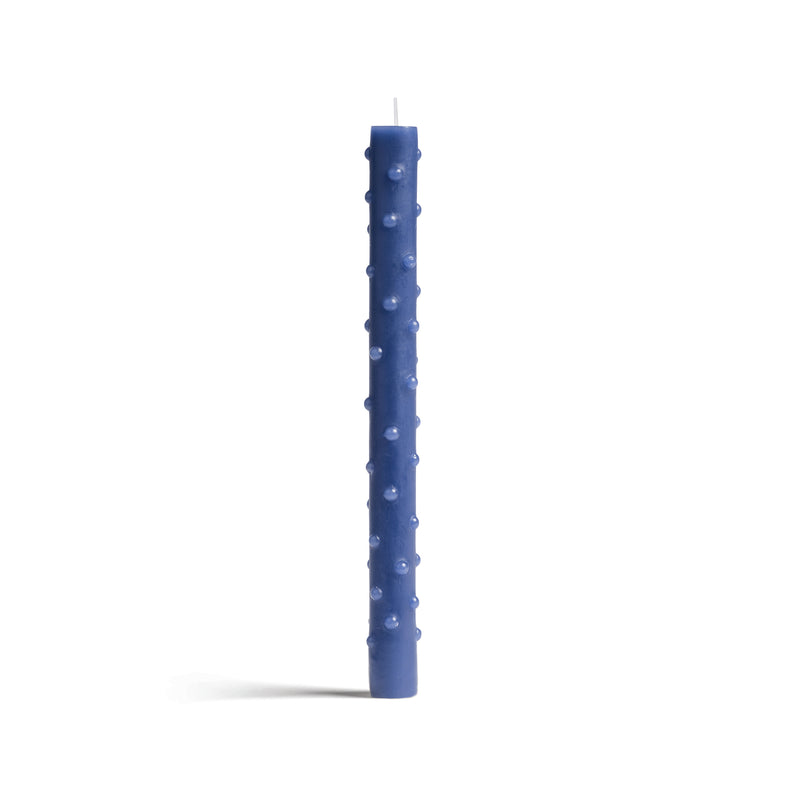 A tall, slender blue candle with a textured dotted surface stands against a white background. Made by &Klevering, this elegant piece features a visible wick at the top.