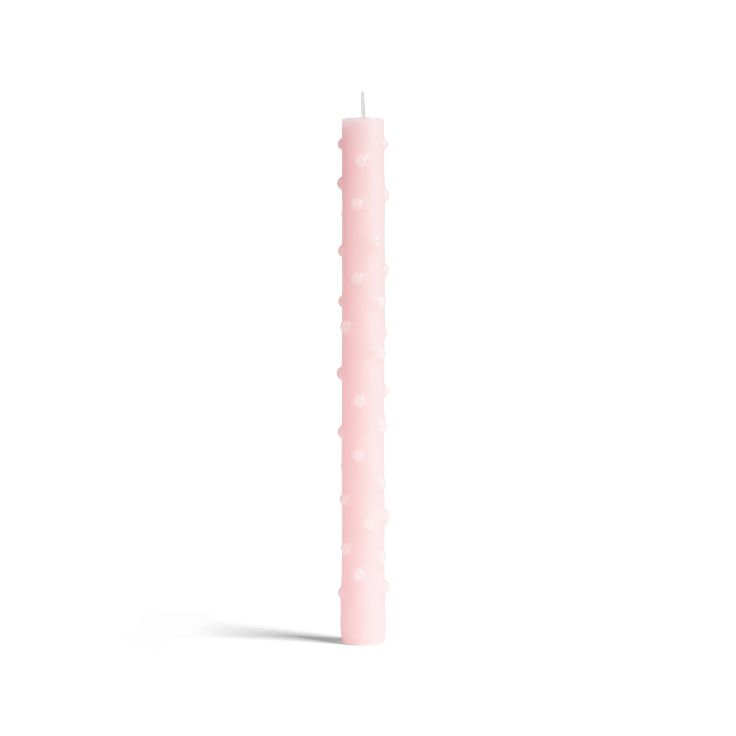 A tall, pink taper candle with a textured pattern of small, raised dots is showcased against a plain white background, exemplifying &Kleverings meticulous craftsmanship.