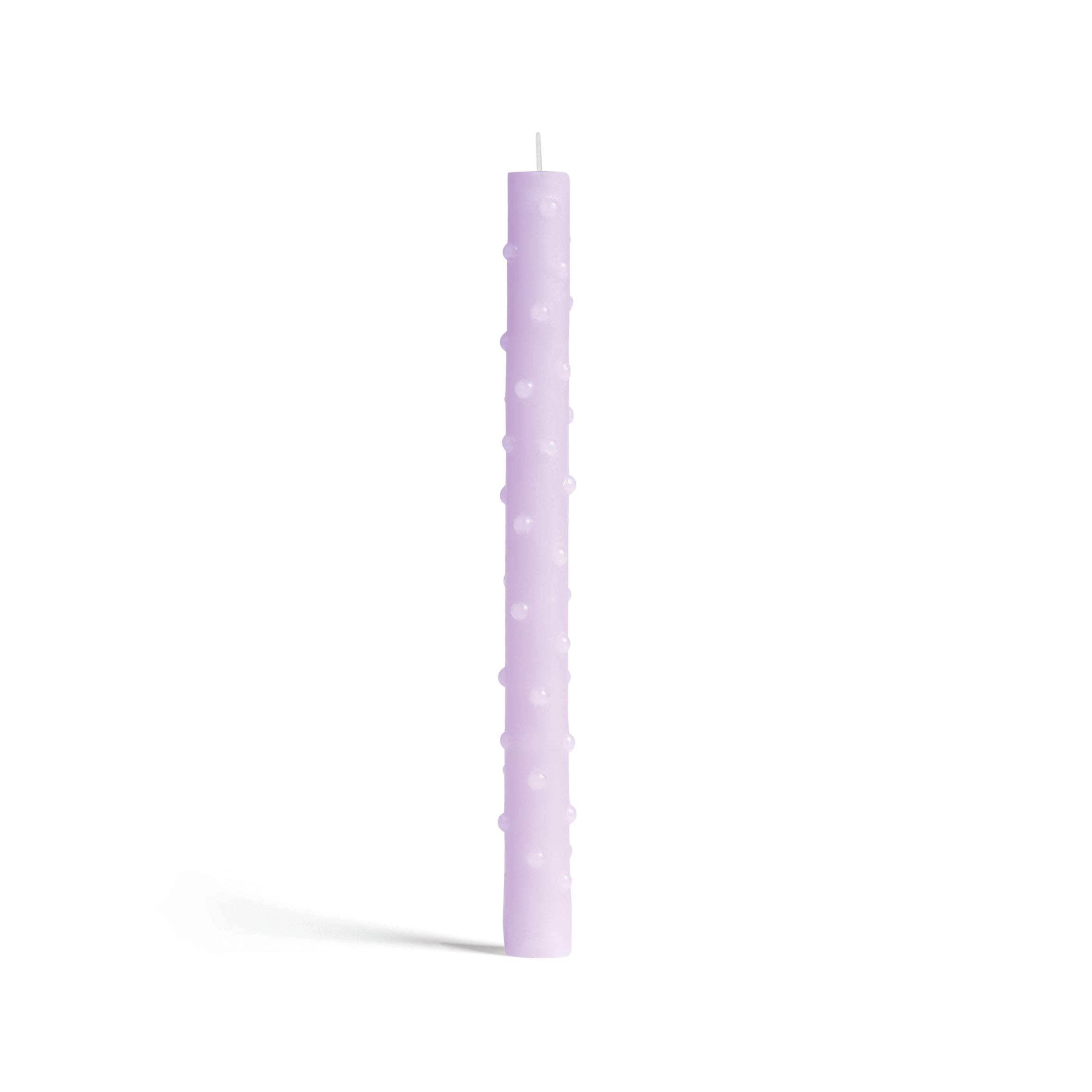 A tall, slender lavender &Klevering candle with raised polka dots stands unlit against a white background, casting a subtle shadow. Crafted with care, this charming piece now comes in green and ensures top quality craftsmanship.
