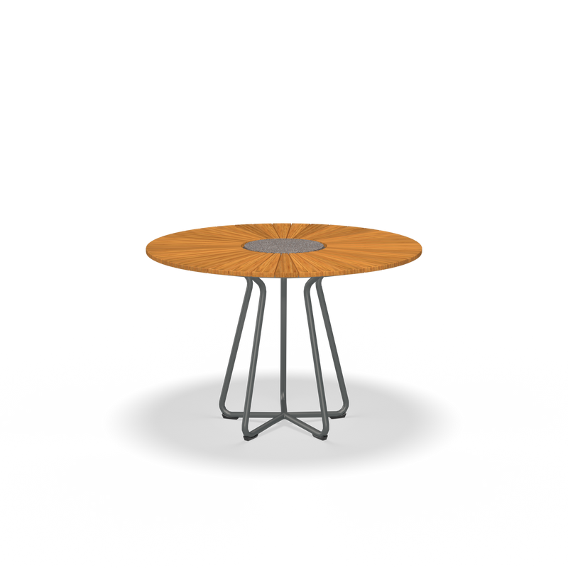 The Circle Table by Houe is a round wooden piece featuring a central geometric pattern and an innovative base made from intertwined powder-coated aluminum legs.