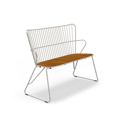 The Paon Bench by Houe features a modern Scandinavian design with a sleek white metal frame and wooden seat, complemented by a vertical slat backrest and angled metal legs, all highlighted against a black background.
