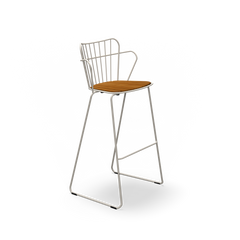 The Paon Barstool by Houe features a stylish minimalist design with a metal frame and wooden seat. It boasts a high back with vertical bars, angled legs with a footrest, and its Scandinavian-inspired aesthetic blends beautifully with the black frame and natural-finish seat.