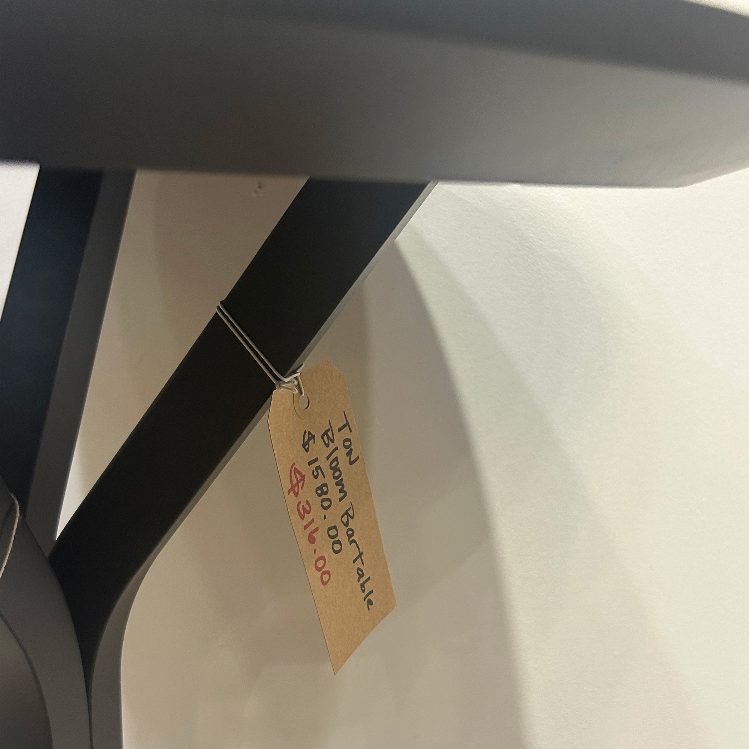 Bloom Bar Table Round - Sale showing black metal frame and price tag hanging on leg of table.