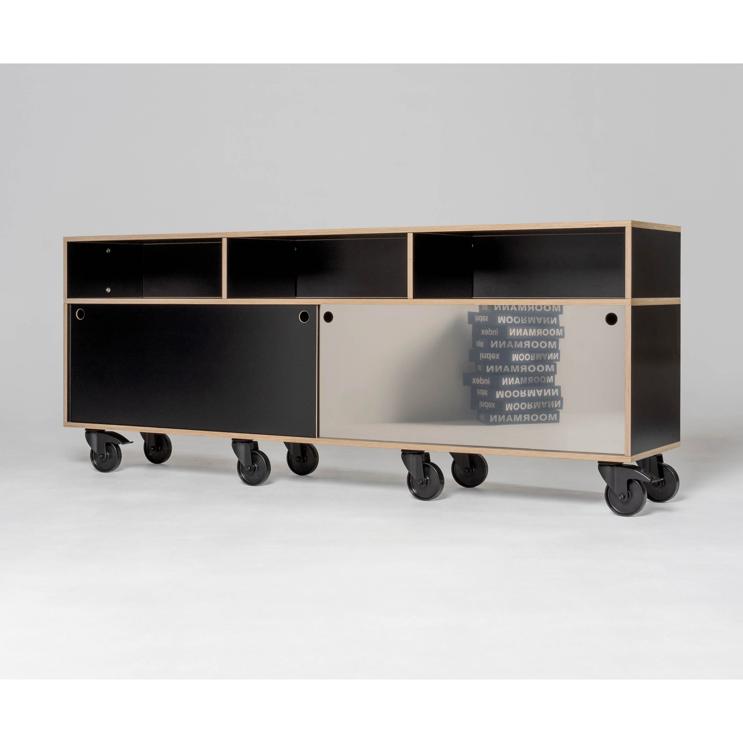The Egal Rockboard by Moormann is a modern, minimalist sideboard featuring open shelves and sliding doors in black and reflective finishes. It rests on six large black caster wheels against a plain grey background.