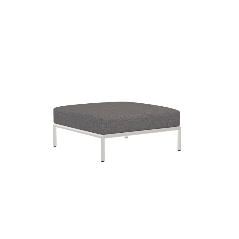 The Level Ottoman by Houe is a modern piece featuring a square design with dark fabric cushions and sleek metal legs made from powder-coated aluminum, all set against a solid black backdrop.