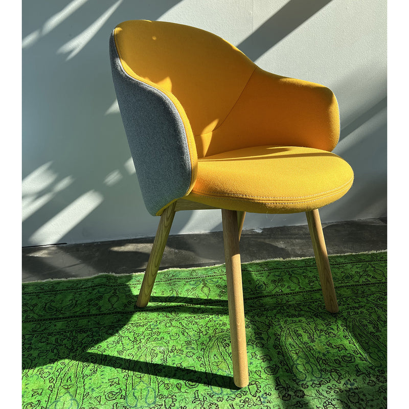 The TON Armchair Albu - Sale showcases an ergonomic design with a yellow seat and gray backrest on wooden legs, elegantly set on a green patterned rug as sunlight casts playful shadows.
