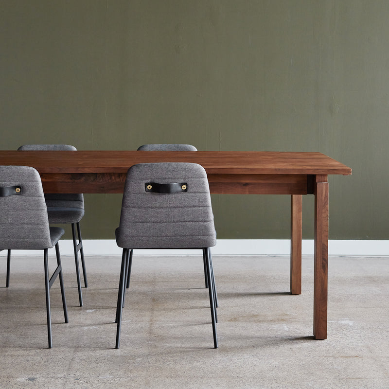 A Gus Modern Annex Extendable Dining Table with four gray upholstered chairs is placed on a light floor, against a plain olive-green wall.