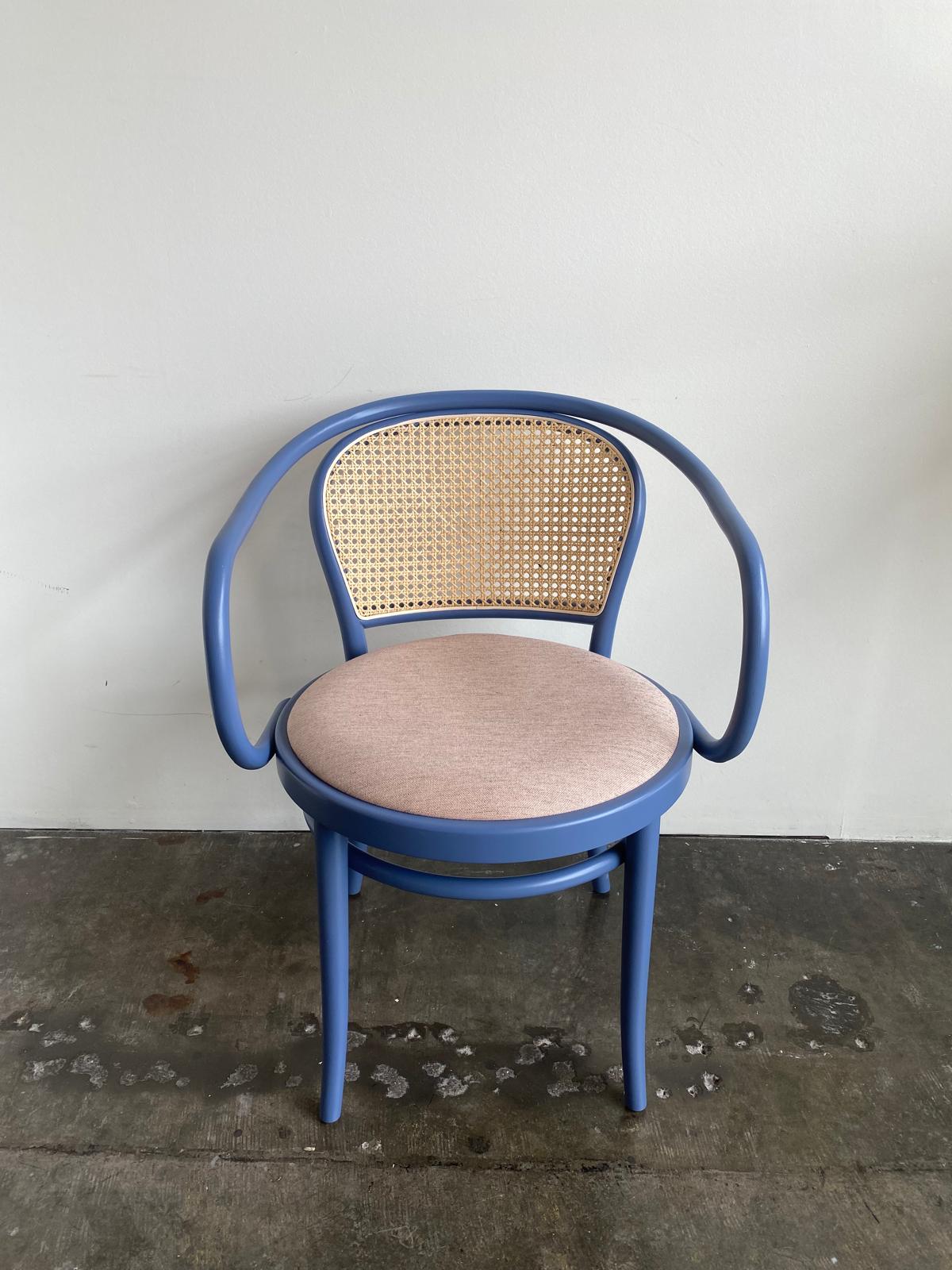 The Armchair 33- Sale by TON features a classic blue wooden design with a circular cushioned seat and curved backrest with a woven cane pattern, seamlessly fitting against white walls on concrete floors for versatile use in any space.
