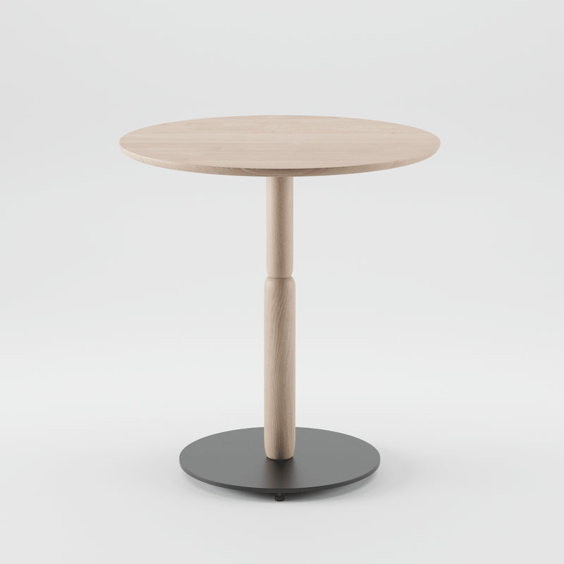 The Bistro A Table by Artisan is a minimalist round wooden table made from solid, eco-friendly materials. It features a central support and a sleek black circular base, all set against a plain white background.