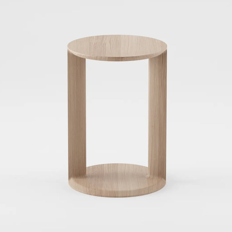 The BOAZ Sidetable by Artisan is a minimalist wooden side table crafted from solid wood featuring a circular top and base connected by three vertical panels. Its light wood, enhanced with natural oils, has a smooth finish that provides a sleek and modern look against a plain white background.