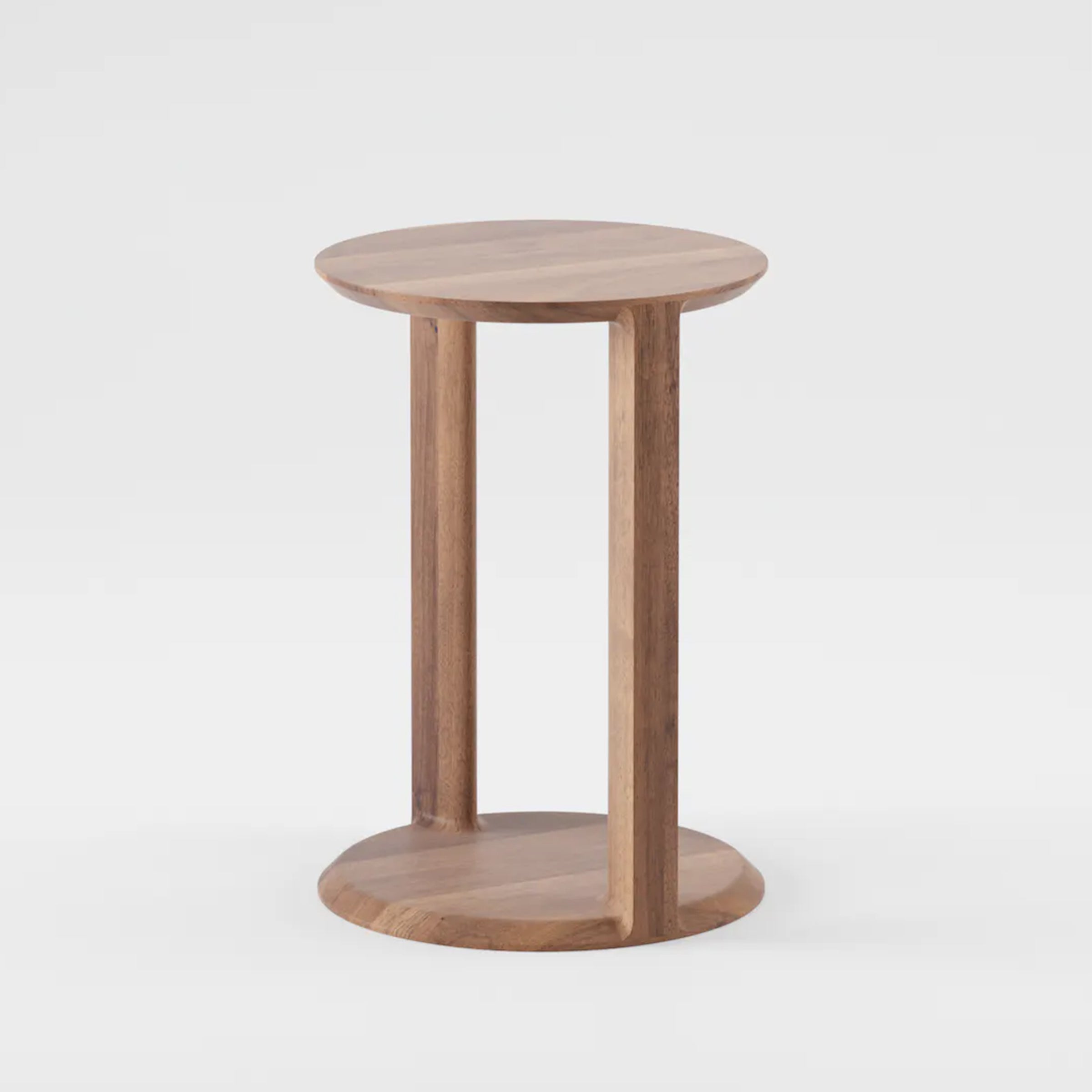 The BOAZ Sidetable by Artisan is a round, solid wood piece with a smooth top and bottom connected by three vertical supports. It features a light, natural finish enhanced with eco-friendly materials and is shown against a plain white background.