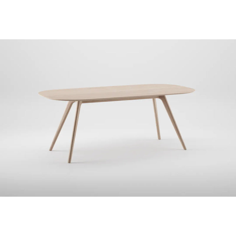 The COCO Table by Artisan is a minimalist piece made from solid wood with a smooth, rectangular top and rounded edges. Its four slender, outward-angled legs are set against a plain white background, showcasing environmentally-friendly materials.
