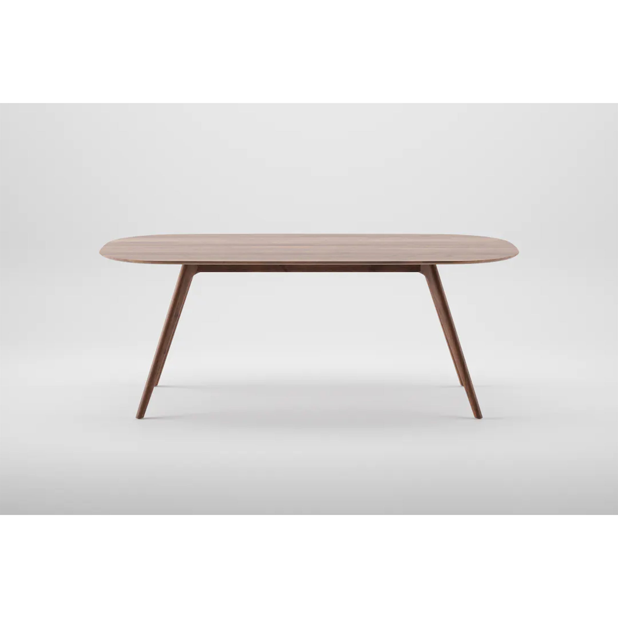 The COCO Table by Artisan is a minimalist wooden dining table made from solid wood, showcasing an oval top and sleek tapered legs. It is elegantly finished with natural oils and set against a plain white background.