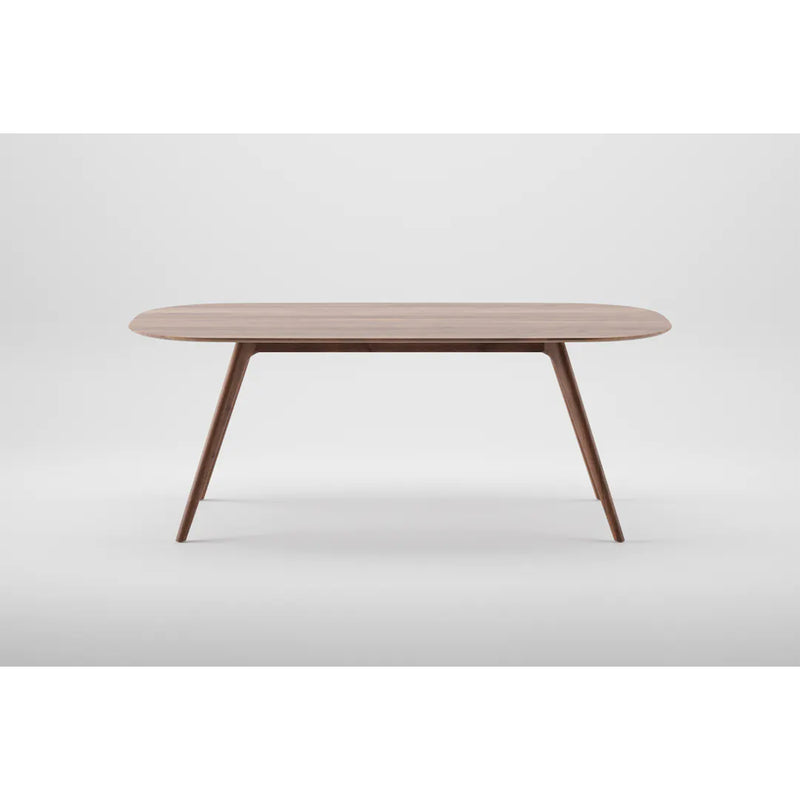 The COCO Table by Artisan is a minimalist wooden dining table made from solid wood, showcasing an oval top and sleek tapered legs. It is elegantly finished with natural oils and set against a plain white background.