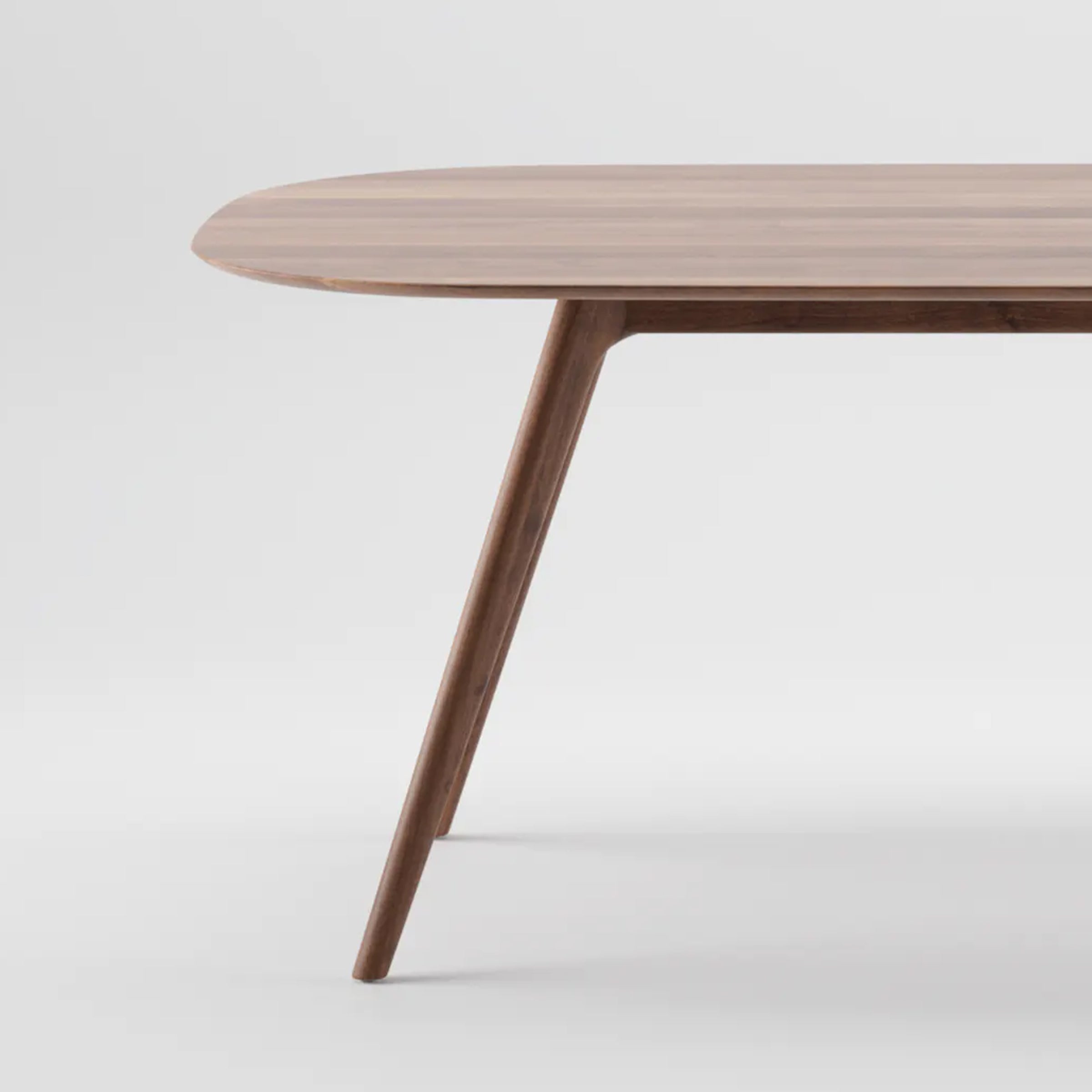 A close-up of the COCO Table by Artisan features a solid wood construction with an oval top and four slender, angled legs. The tables smooth surface is enriched with natural oils, highlighting its rich grain against a plain white background.