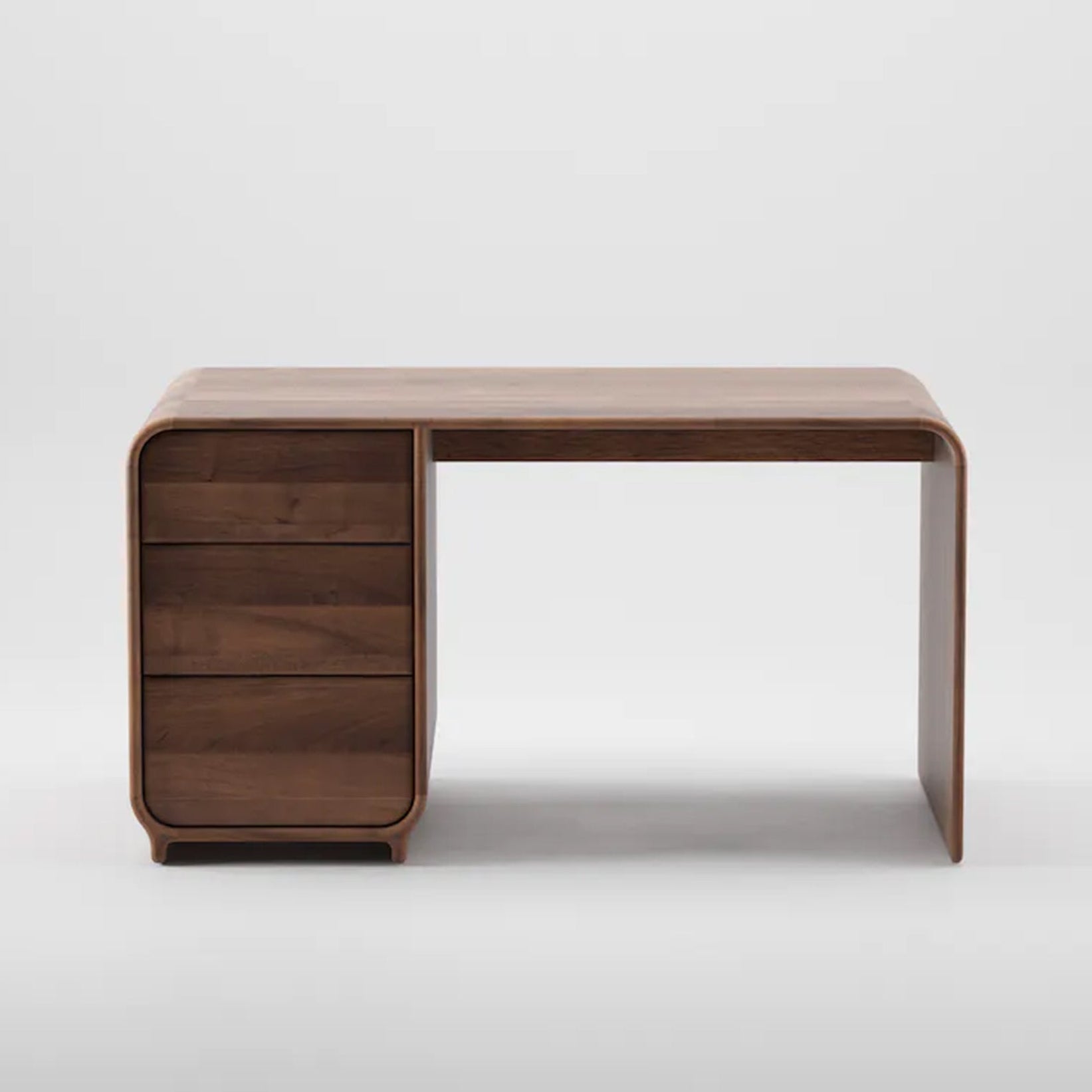 The ENY Working Desk by Artisan is a modern, curved design crafted from solid wood and finished with natural oils. It has a smooth top and four polished shelves on the left, set against a plain white background.