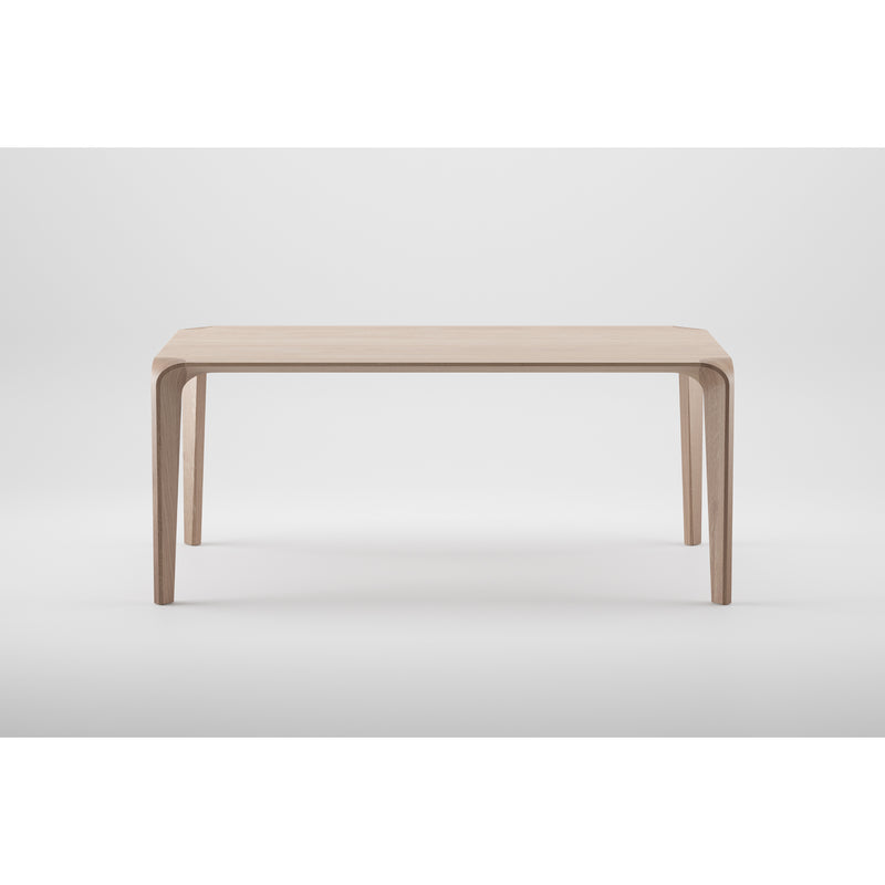 The Artisan FLOW Table is a minimalist wooden table crafted from solid wood with a natural oil finish, featuring sharp, clean lines and gracefully tapered legs. Its neutral white background enhances its modern, eco-friendly design.