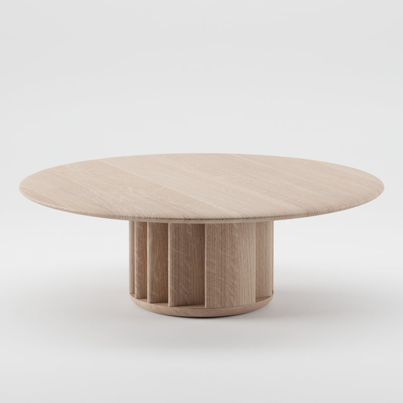 The GRID Coffee Table by Artisan features a round wooden top with a unique cylindrical base made of vertical panels, crafted from sustainable materials and finished with a light, natural touch. Set against a plain white background.