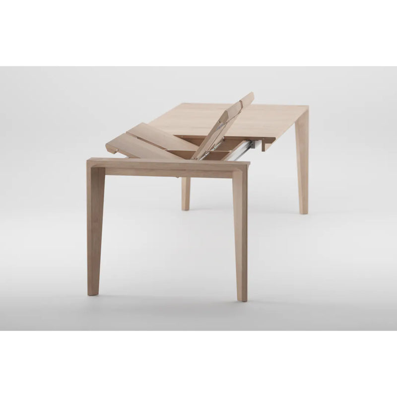 The HANNY Extension Table by Artisan, crafted from solid wood, showcases its extension mechanism with a partially lifted section. Set against a plain white background, the tables sleek design is enhanced by its natural wood texture.