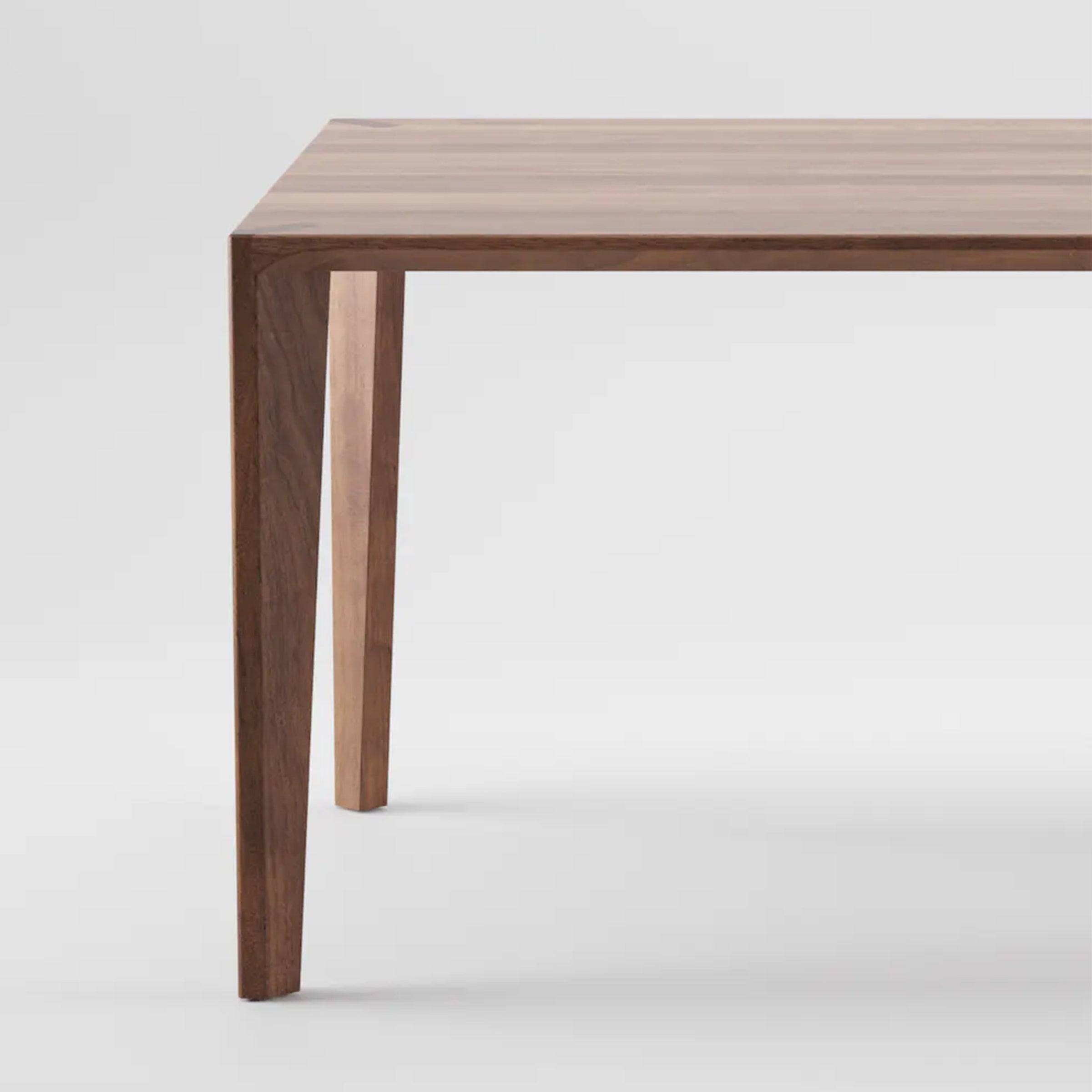 A close-up showcases the Artisan HANNY Extension Table, revealing a smooth, natural wood texture. Made from eco-friendly dark solid wood with a simple rectangular design, only part of its tabletop and two legs are visible against a plain background.