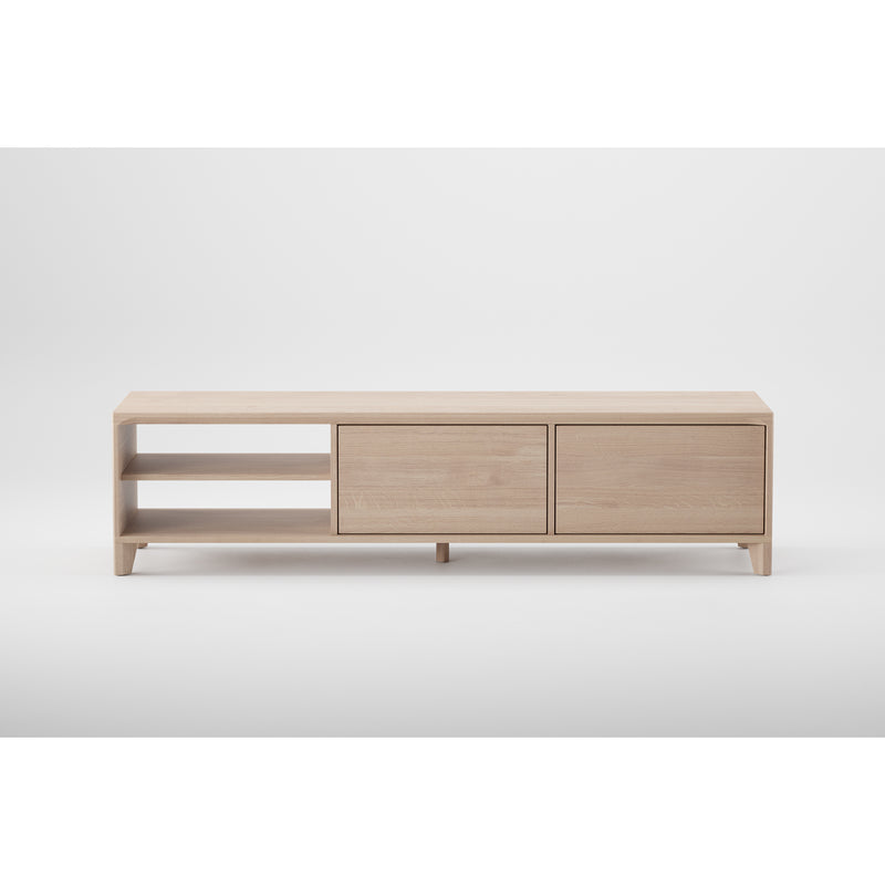 The HANNY Lowboard by Artisan is a minimalist, light wood TV stand crafted from solid wood. It features a natural texture with two open shelves on the left and two closed cabinet doors on the right, all elevated on small legs against a plain white background.