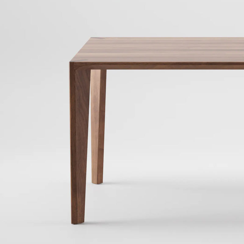 The HANNY Table by Artisan showcases a close-up of its corner featuring a minimalist design with clean, sharp edges. Crafted with natural oils, its four visible legs beautifully accentuate the wood grain against a plain white background.