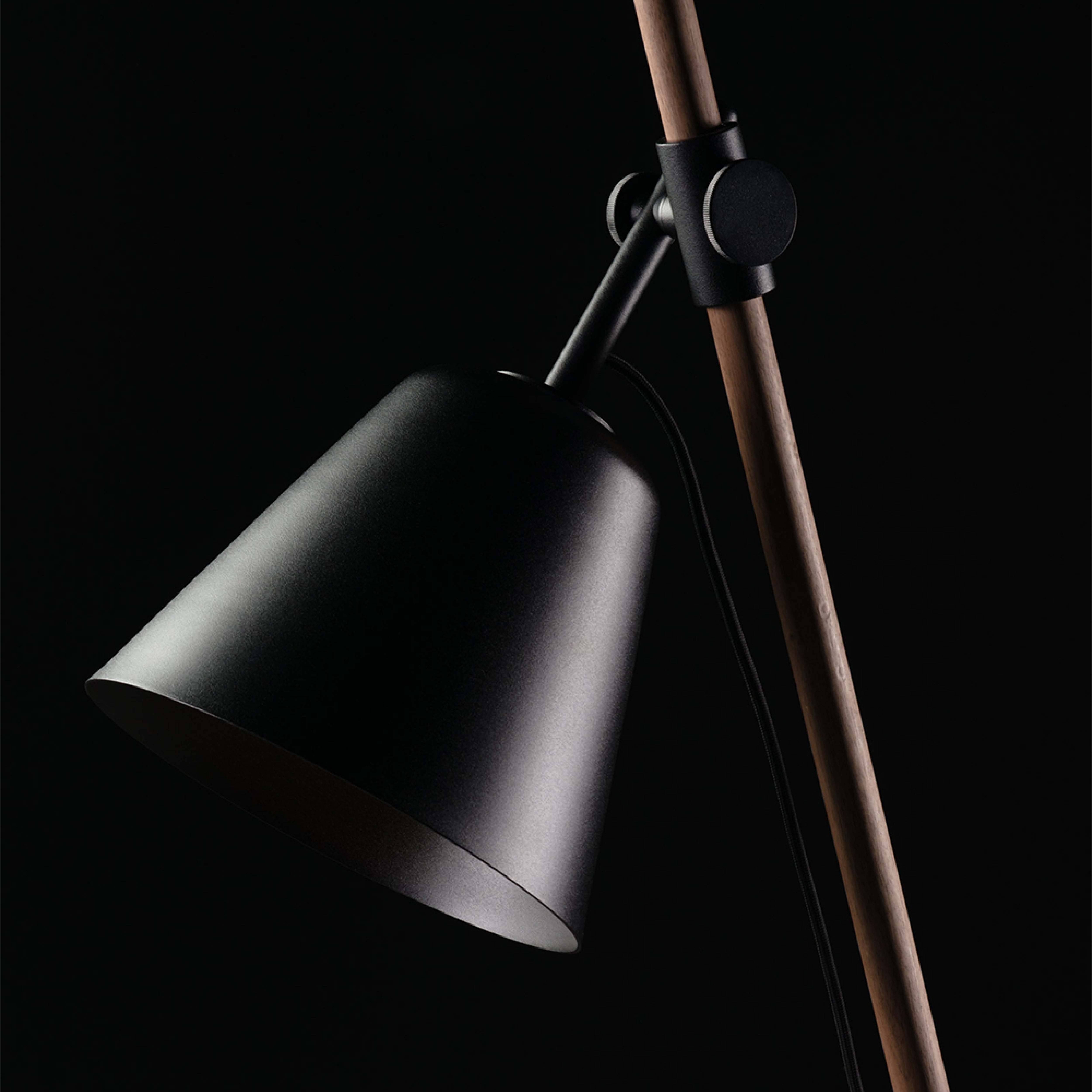 Close-up of the Artisan INSERT Floor Lamp with a modern black, cone-shaped shade against a dark background. Made from eco-friendly solid wood and finished with natural oils, it features a round swivel joint for an elegant, minimalist look.