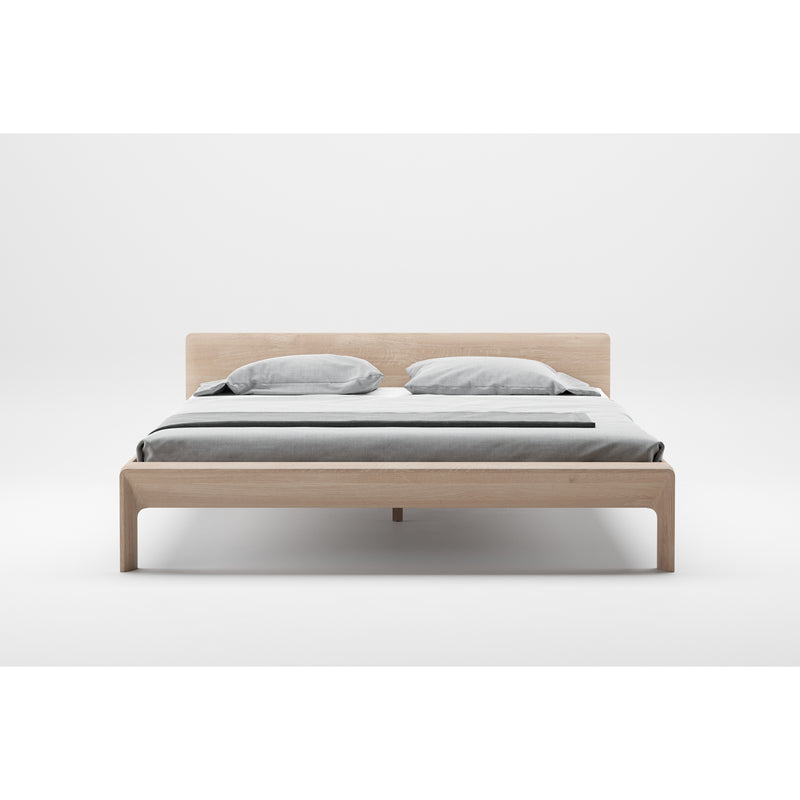 The INVITO Bed by Artisan features a minimalist design with a light wood frame and simple headboard, highlighting its natural wood texture. Its elegantly dressed in gray bedding with two pillows and a matching duvet, while the surrounding white space accentuates its artisan craftsmanship.