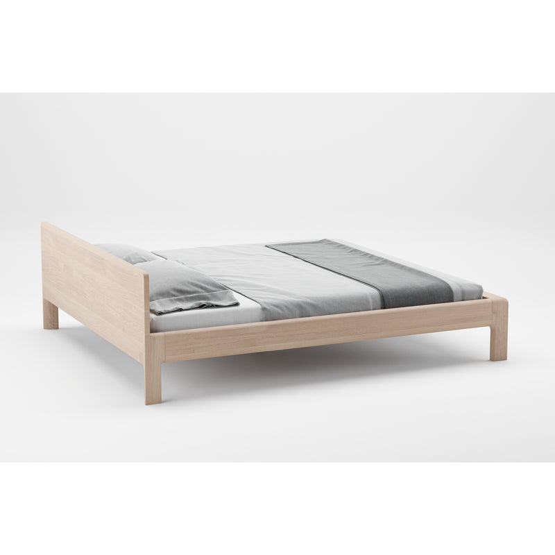 The Artisan INVITO Bed, made from eco-friendly wood, boasts a minimalist frame with a simple headboard. Its natural texture is complemented by white and gray bedding, enhancing the clean modern aesthetic against a neutral backdrop.