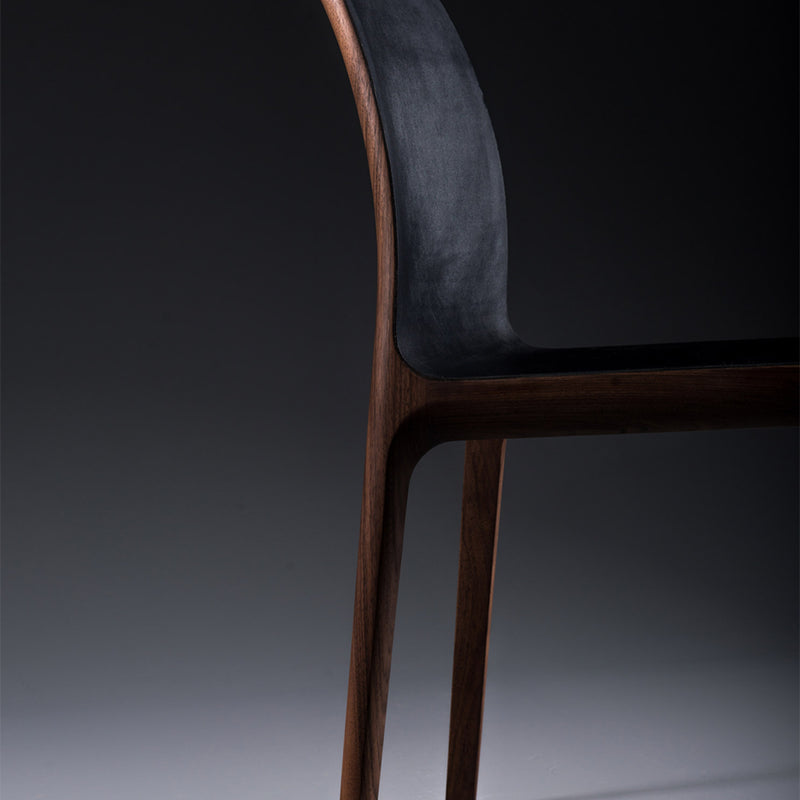 The INVITO Chair by Artisan showcases sleek solid wood legs and a curved backrest. The lighting highlights its elegant design against a dark background, emphasizing its use of environmentally-friendly materials.