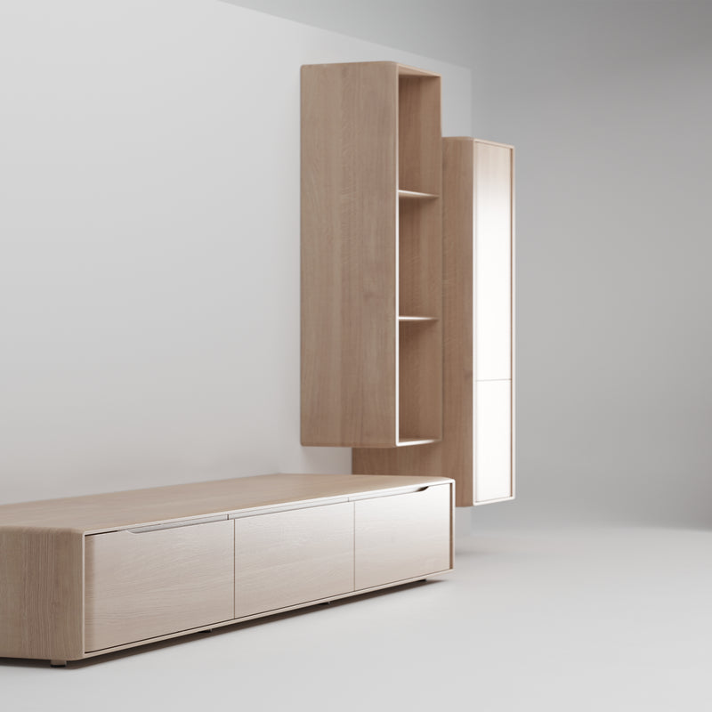 The INVITO MS Lowboard by Artisan is paired with a light gray wall, featuring a low cabinet with three doors and two tall, narrow wall-mounted cabinets with open shelves. The sleek design highlights clean lines and natural solid wood finishes.