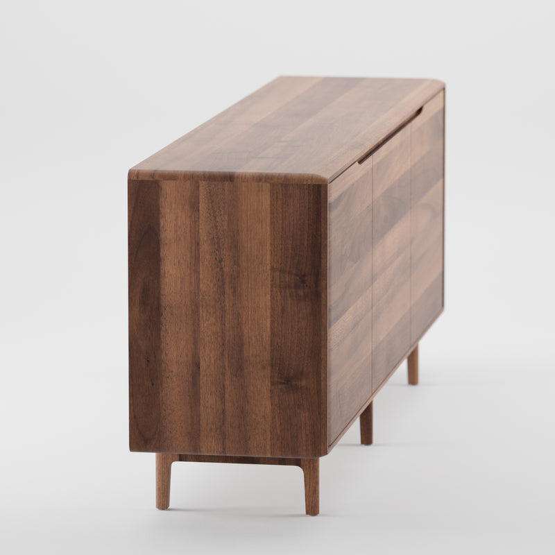 The INVITO Sideboard by Artisan features a minimalist design with clean lines and a rich brown finish. Crafted from solid wood using natural oils, it stands on four short legs with a seamless surface, emphasizing its meticulous craftsmanship from the side view.